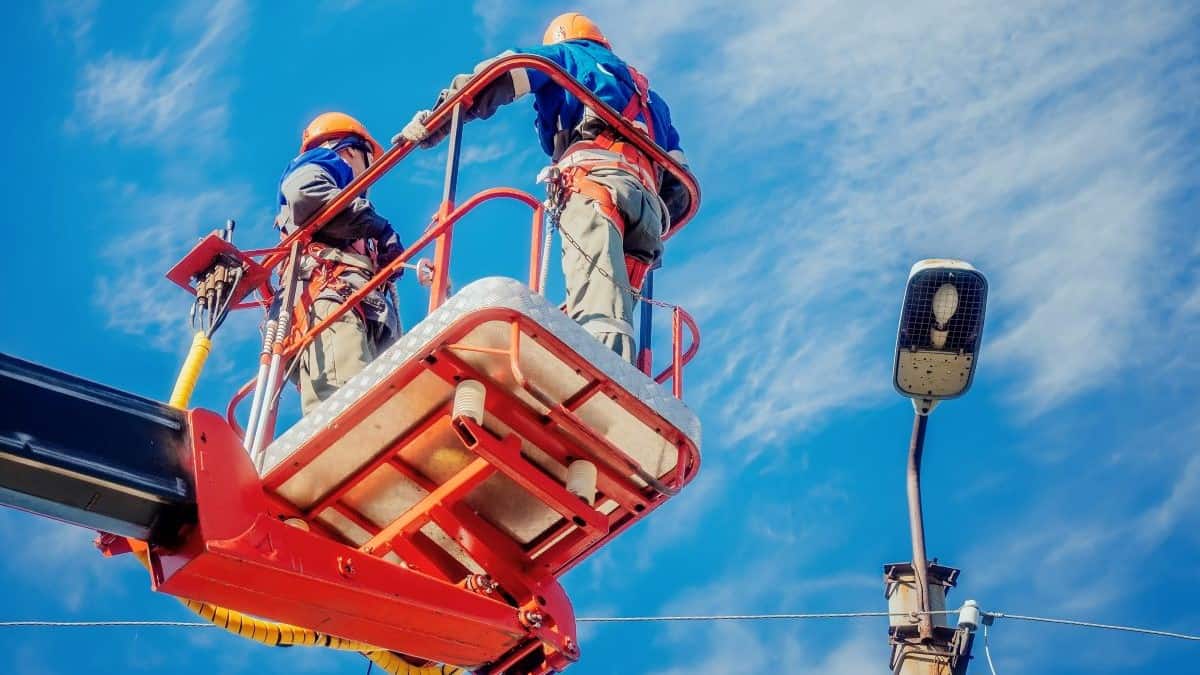 aerial lift certification represented by two electricians in hard hats using an aerial lift to repair a streetlight